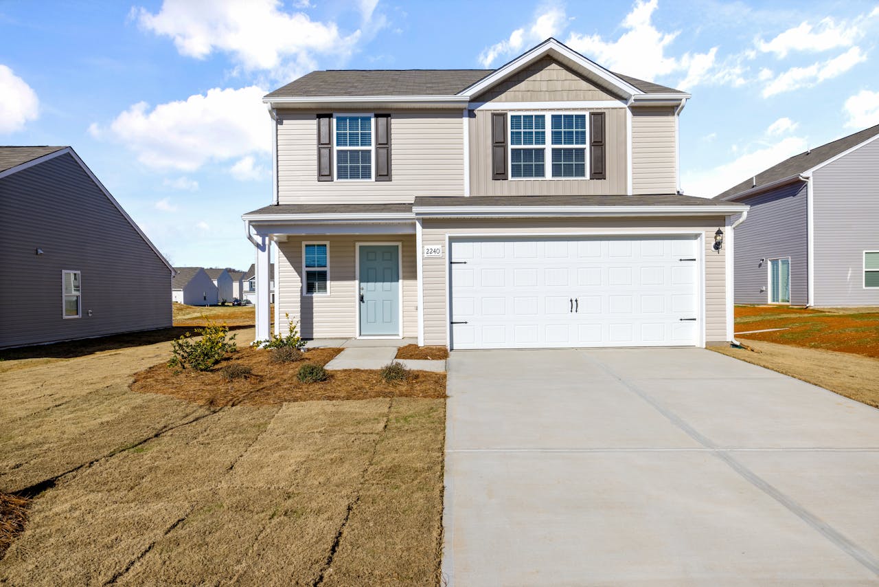 Two-story suburban house with large driveway and clear blue sky.