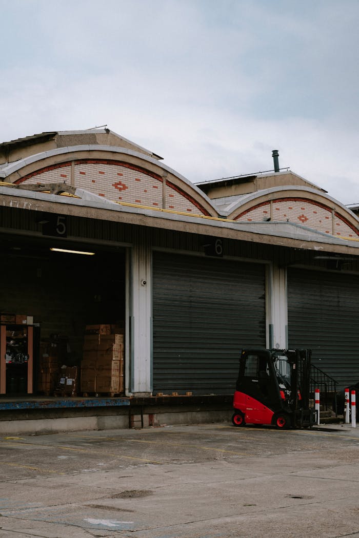 About A red forklift parked at a warehouse loading dock with closed garage doors.