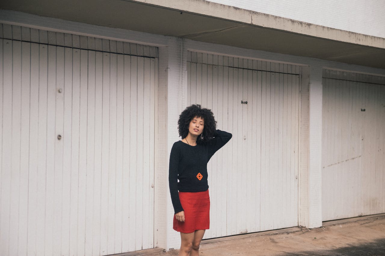 Fashionable woman in red skirt and black top posing outdoors with white garage doors in São Paulo.